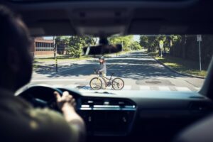 This is an image of a driver slowing to a stop while a child on a bike crosses in the crosswalk.